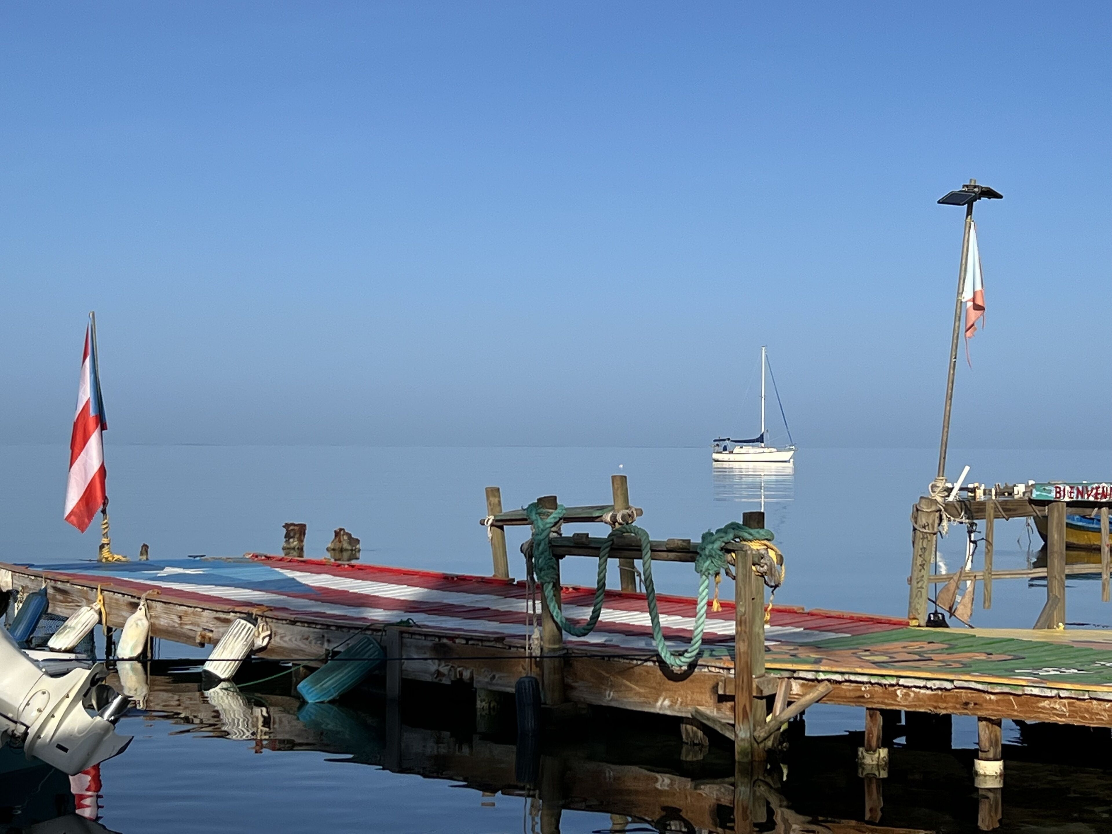 A wooden pier with a flag, a sailboat, and a lifebuoy.