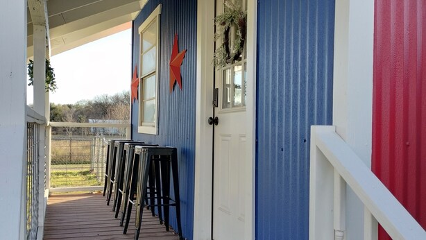 Une véranda dotée d’un plancher en bois, d’une balustrade blanche et d’un mur bleu orné d’une étoile rouge.