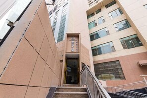 Una entrada de edificio con un letrero, una escalera y una barandilla metálica.