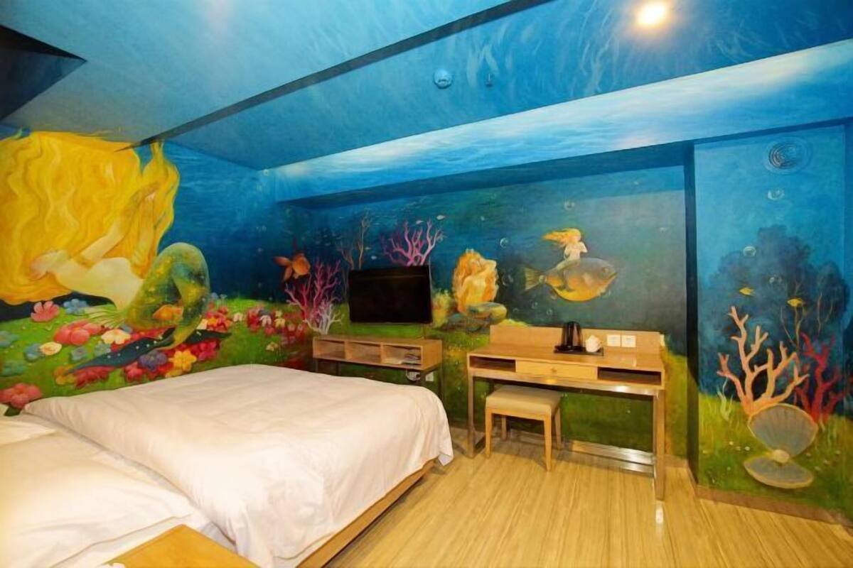 A bedroom with an underwater-themed mural, a bed, a desk, and a television.