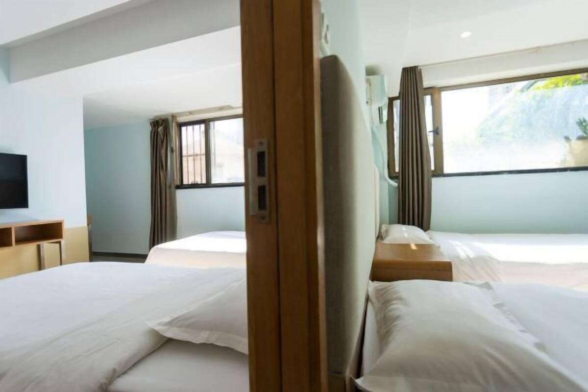 A hotel room with two beds, a TV, and a window with a view of greenery.