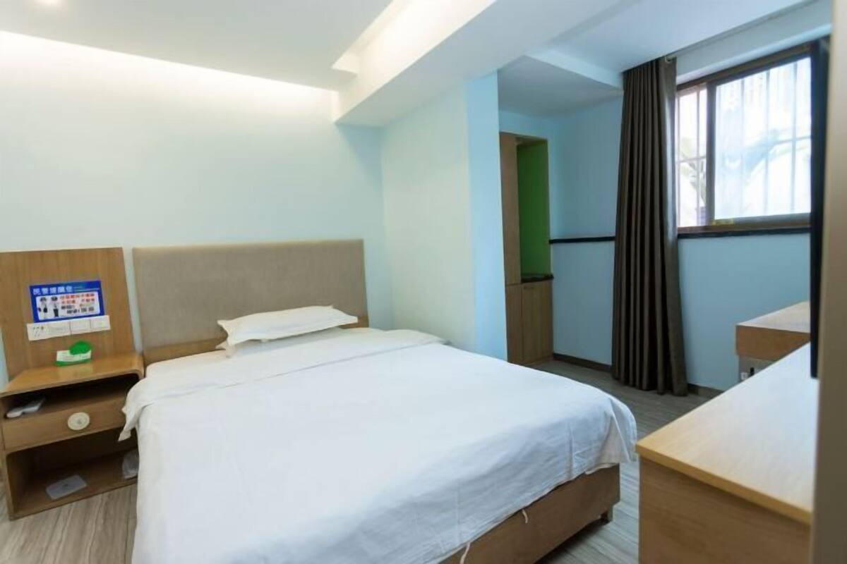A hotel room with a single bed, a wooden nightstand, a desk, and a window with curtains.