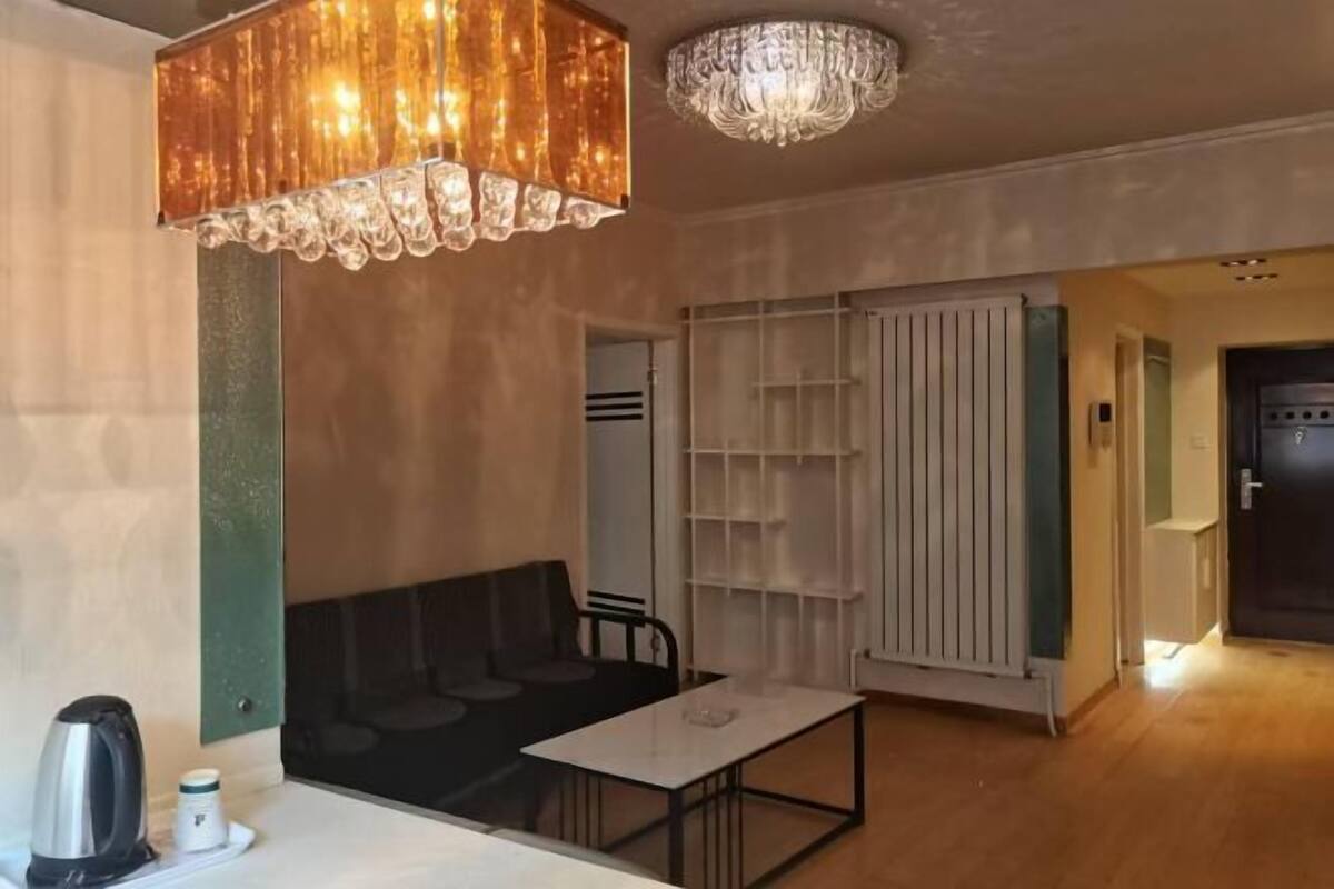 A room with a table, chairs, a sofa, a radiator, and a chandelier.