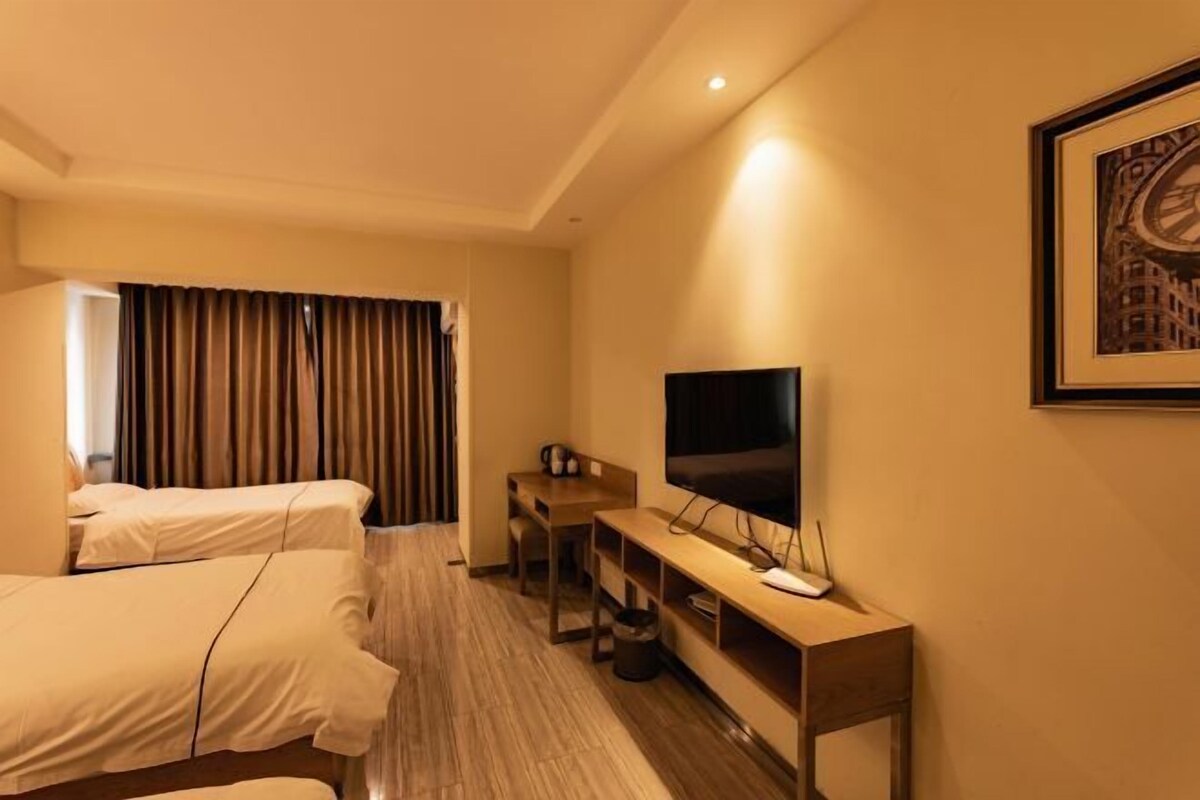 Habitación de hotel con dos camas, un escritorio con televisor y un cuadro en la pared.
