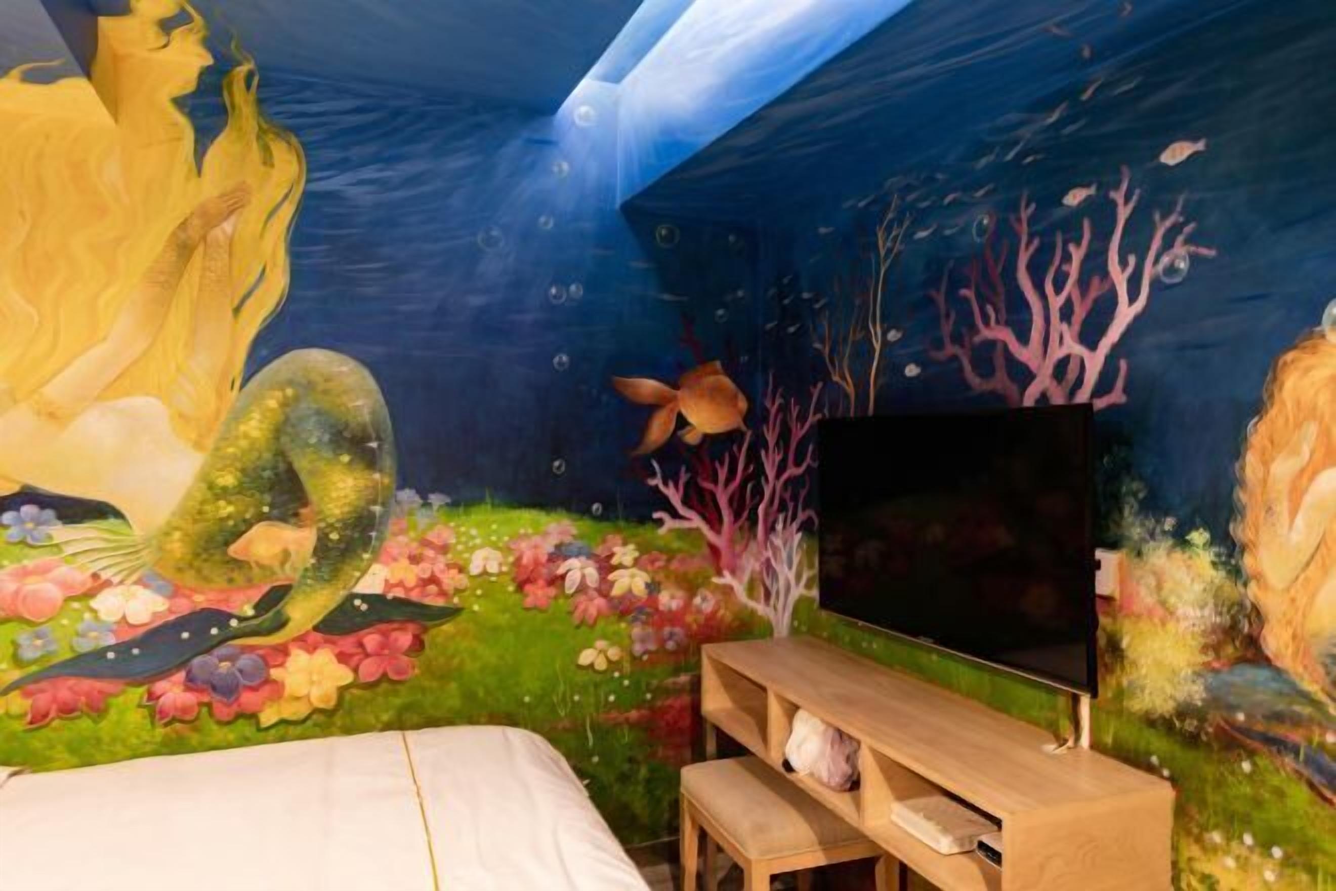 A bedroom with a mural, a bed, a TV, and a wooden bench.
