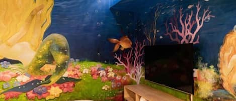 Une chambre avec une fresque murale, un lit, une télévision et un banc en bois.