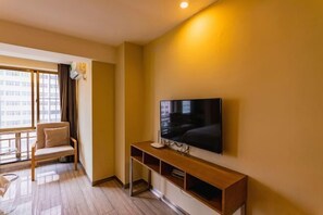 Una habitación de hotel moderna con un televisor de pantalla plana grande montado en la pared, una mesa consola de madera, un sillón cómodo y un ventanal con vistas a la ciudad.