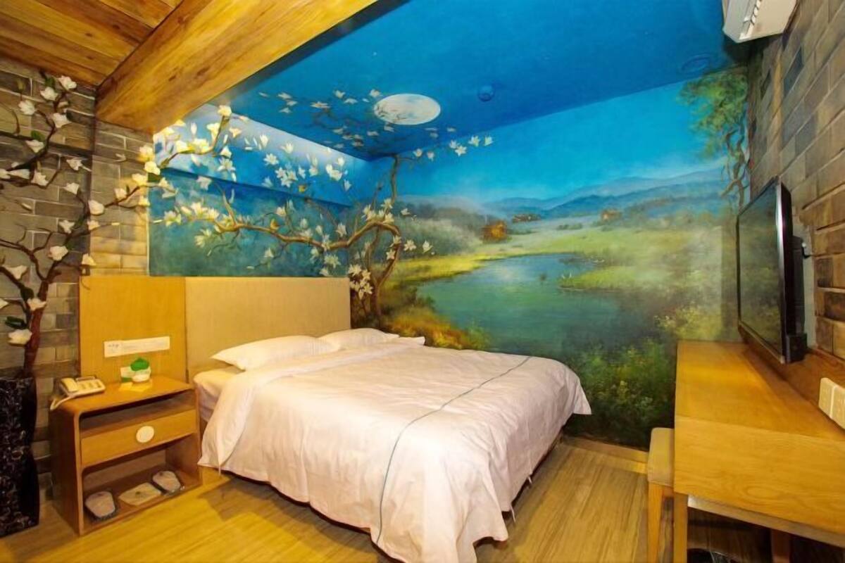 A bedroom with a mural of a landscape, a bed, a nightstand, and a wooden desk.