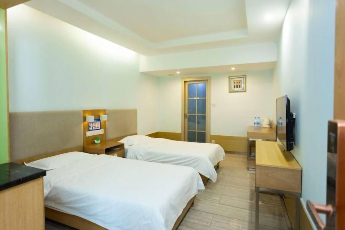 A hotel room with two beds, a desk, a TV, and a door.