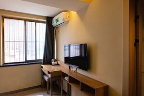 Una habitación con una televisión de pantalla plana montada en la pared, un escritorio de madera y una ventana con cortinas.