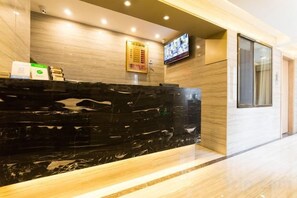Un área de recepción con mostrador de mármol, televisor montado en la pared y puerta de madera.