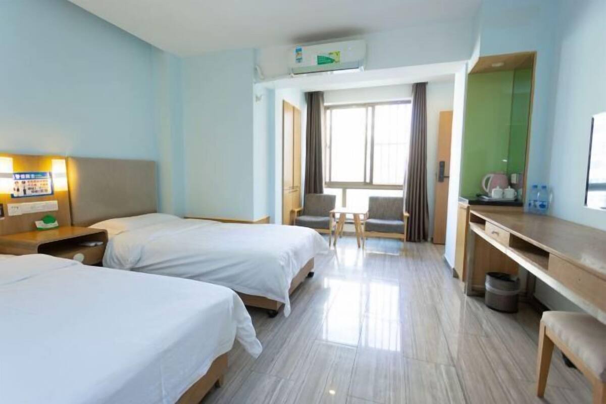 A hotel room with two beds, a desk, a chair, a small table, and a window.