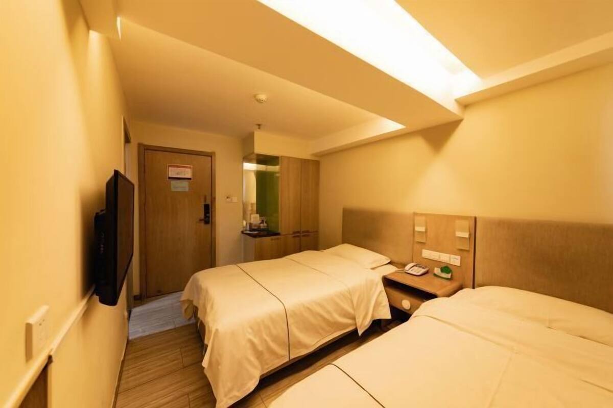 A hotel room with two beds, a television, a bedside table with a phone, and a mirror.