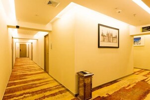 Un pasillo de hotel con piso alfombrado, un cesto de basura y cuadros en la pared.