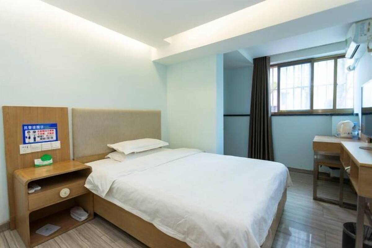 A hotel room with a bed, a desk, a chair, a nightstand, and a window.