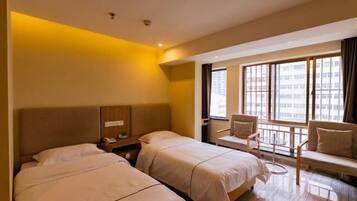 A hotel room with two beds, a seating area with a chair and a small table, and a large window offering a city view.