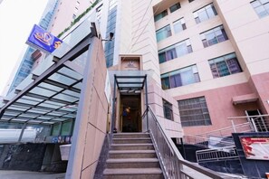 Entrada de un edificio con fachada de vidrio, una escalera y un letrero.