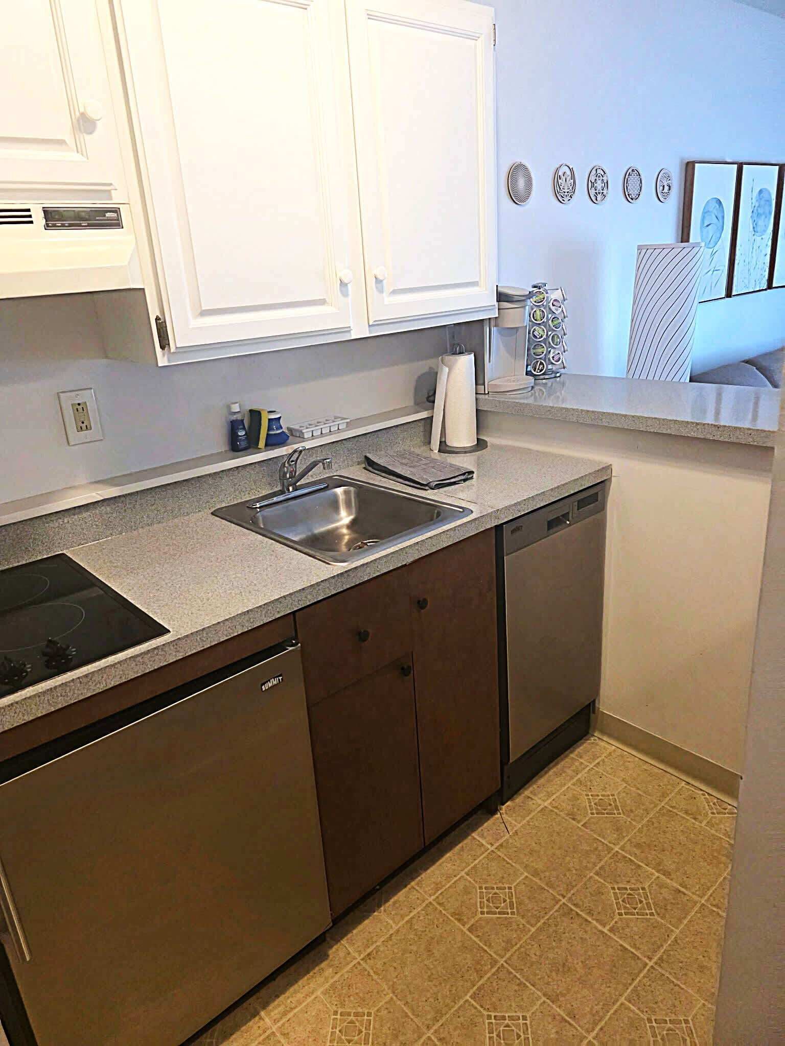 A kitchen with white cabinets, a stainless steel sink, a dishwasher, and a countertop with a paper towel dispenser.