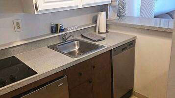 A kitchen with white cabinets, a stainless steel sink, a dishwasher, and a countertop with a paper towel dispenser.
