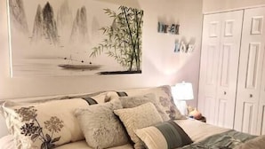 Een slaapkamer met een bed, kussens, een wandlamp en een kledingkast.