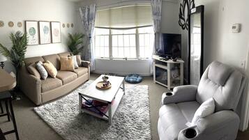 A living room with a beige sofa, a white armchair, a coffee table, and a TV stand with a flat-screen TV.