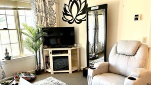 Een woonkamer met een televisie, een bank, een spiegel, een plant en een decoratief wandobject.