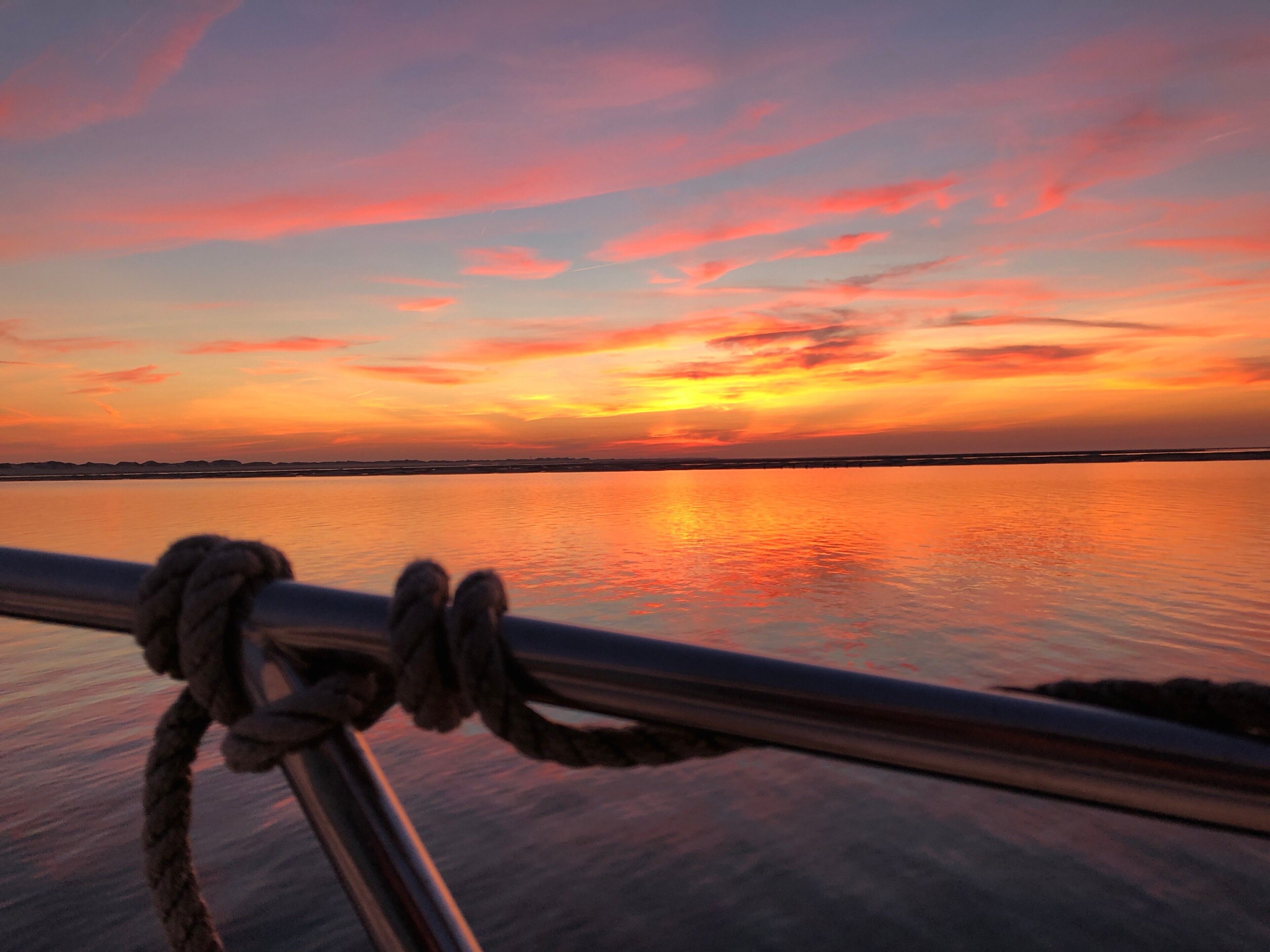 A sunset over a calm body of water with a rope tied to a metal railing in the foreground.