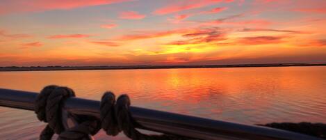 A sunset over a calm body of water with a rope tied to a metal railing in the foreground.