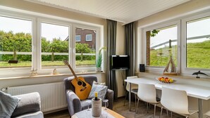 A modern living room with a guitar, a TV, and a dining area with a white table and chairs.