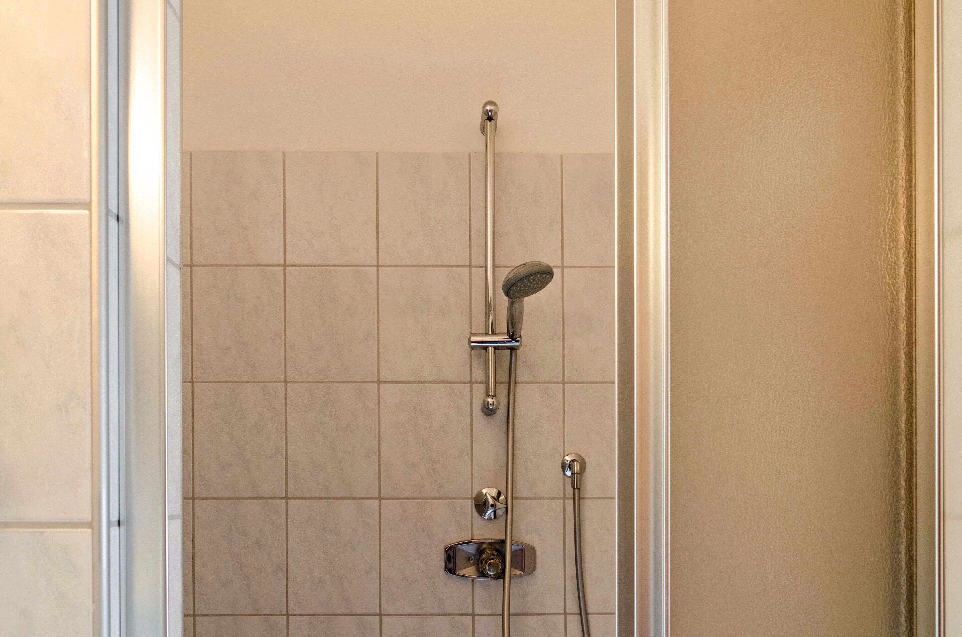 Une douche équipée d’un pommeau de douche à main, d’un robinet mural et d’un panneau de commande.