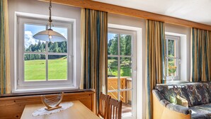 Una habitación con mesa de comedor, sillas de madera, un sofá y ventanas grandes con cortinas.