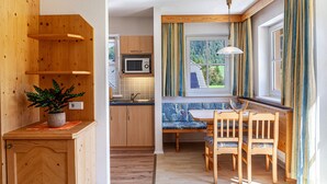 Cocina compacta con armarios de madera, microondas, fregadero y zona de comedor con banco y sillas.