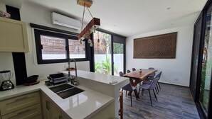 A modern kitchen with a central island, a dining area with a wooden table and chairs, and large windows providing natural light and views of the outdoors. - CASA MEXICANA MODERNA - PISCINA PRIVADA (Tulum)