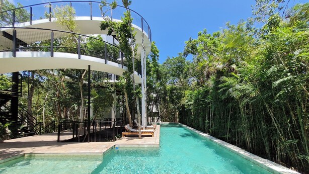 A clear pool surrounded by lush greenery and a modern, multi-level structure with outdoor seating. - CASA MEXICANA MODERNA - PISCINA PRIVADA (Tulum)