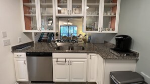 Una cocina con armarios blancos, lavavajillas, cafetera y ventana con vistas.