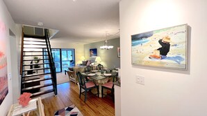 Una sala de estar moderna con comedor, una escalera y un cuadro de playa en la pared.