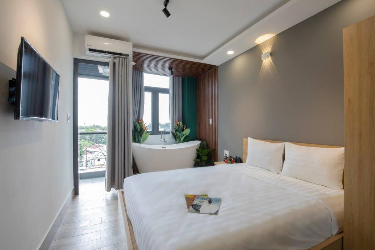 A modern hotel room with a large bed, a built-in TV, a bathroom with a bathtub, and a view of the outdoors.