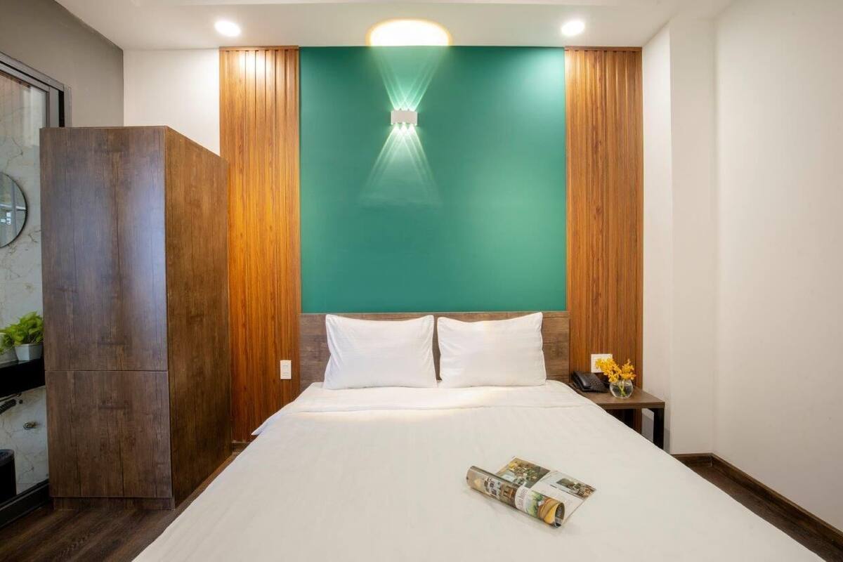 A hotel room with a large bed, wooden paneling, a green accent wall, and a nightstand with a lamp and flowers.