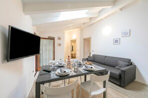 A dining area with a table set for four, a grey sofa, and a TV mounted on the wall.