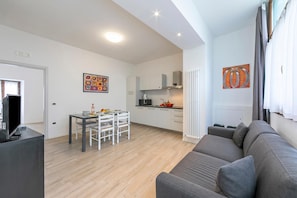 Ein modernes Wohnzimmer mit grauem Sofa, einem Esstisch mit Stühlen, einer Küchenzeile mit Schränken und einer Mikrowelle sowie Kunstwerken an den Wänden.