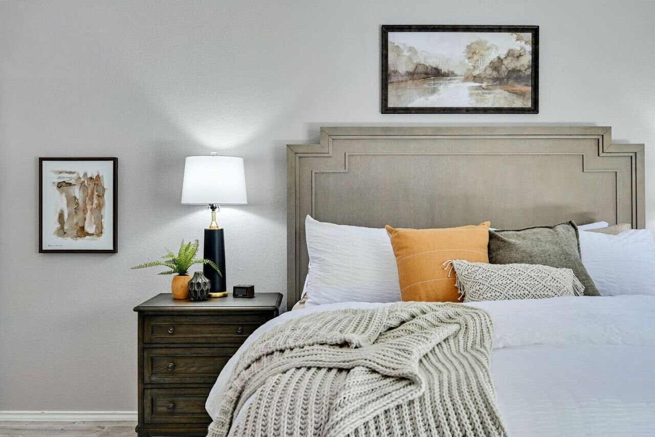 Une chambre à coucher avec un lit, une table de chevet avec une lampe et deux tableaux encadrés accrochés au mur.