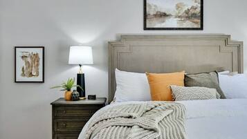 Une chambre à coucher avec un lit, une table de chevet avec une lampe et deux tableaux encadrés accrochés au mur.