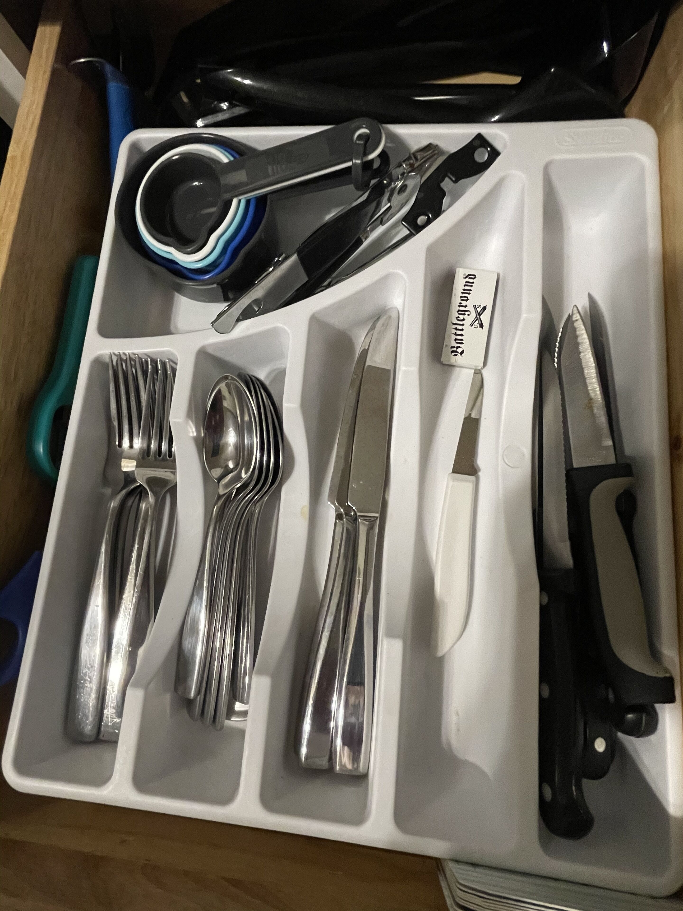 A drawer containing a set of silverware including forks, spoons, a knife, and a pair of scissors.