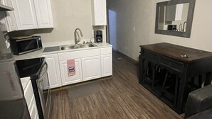 A compact kitchen with white cabinets, a microwave, and a coffee maker. There's a wooden dining table with stools and a small seating area with a couch.
