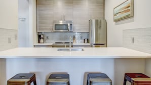 A modern kitchen with stainless steel appliances, a white countertop, and a tiled backsplash. - Modern Interior, Heated Pool Access (Savannah)