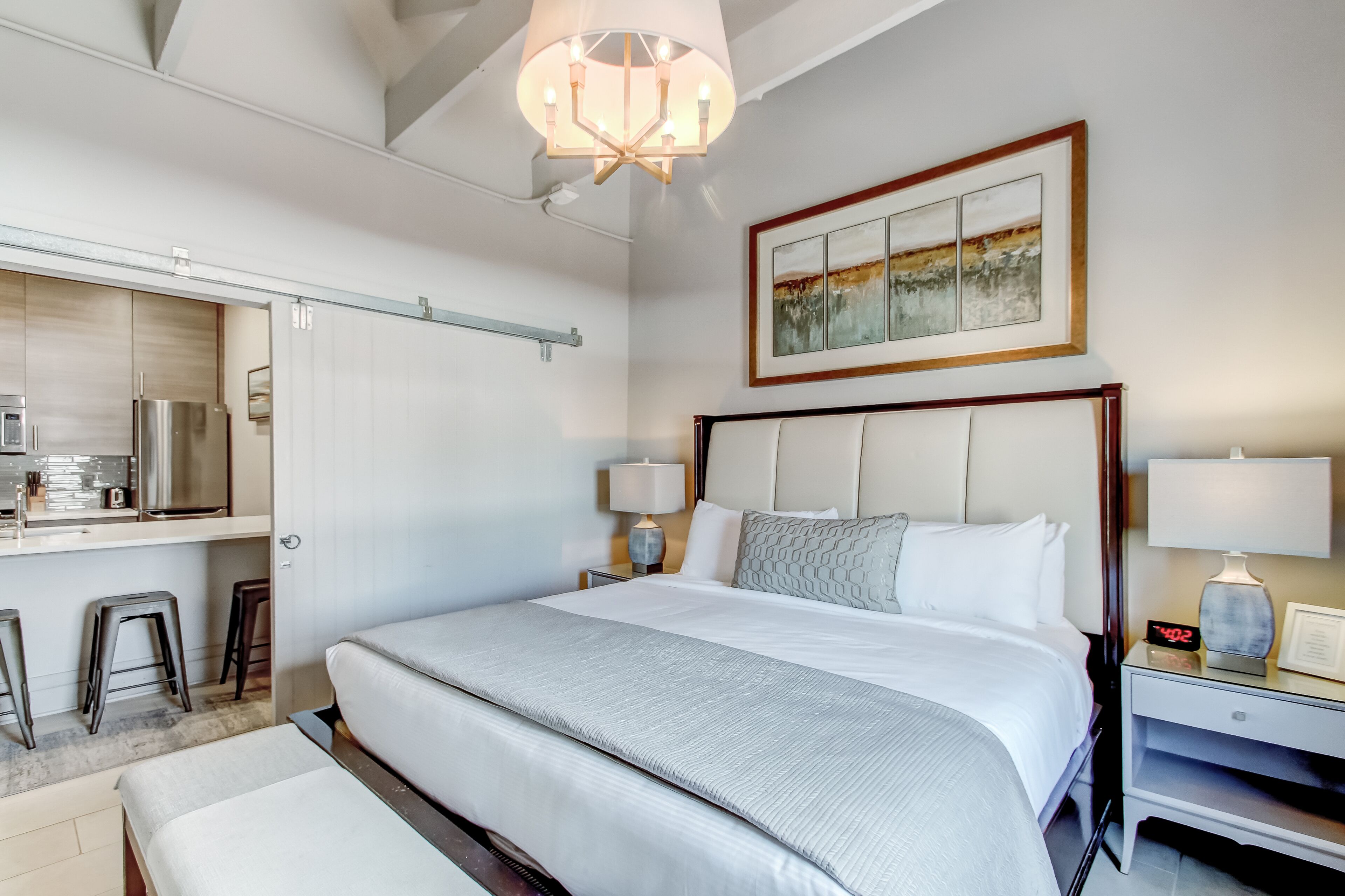 A hotel room with a large bed, a desk with a refrigerator, a dining area, and a painting on the wall.