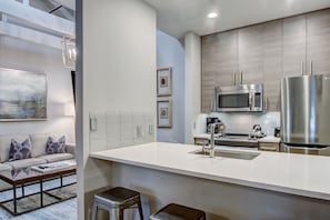 Cozinha moderna com bancada branca, eletrodomésticos de aço inoxidável e micro-ondas embutido.