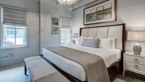 Une chambre à coucher avec un grand lit, des tables de chevet, un banc, un lustre et des œuvres d’art accrochées au mur.