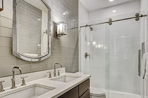 A modern bathroom with a large mirror, two sinks, a glass shower enclosure, and a toilet. - Modern Interior, Heated Pool Access (Savannah)