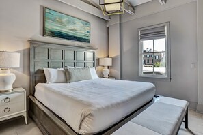 A bedroom with a large bed, two bedside tables with lamps, a painting above the bed, and a window with a view of buildings. - Modern Interior, Heated Pool Access (Savannah)